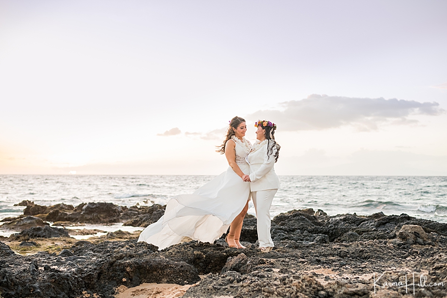 two women just married pose on rocks by ocean
