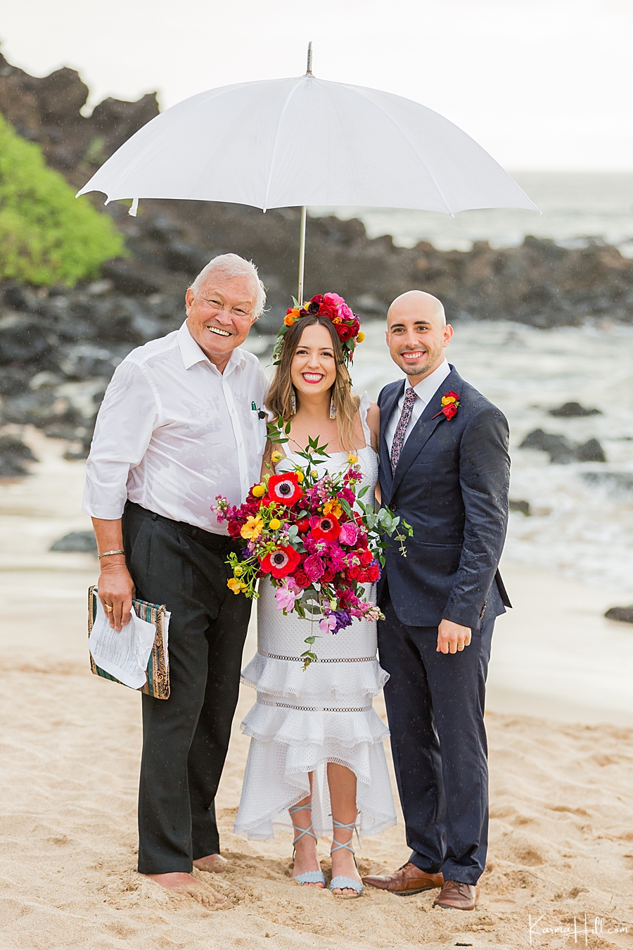 bride and groom pose with minister under umbrella on a rainy beach wedding 