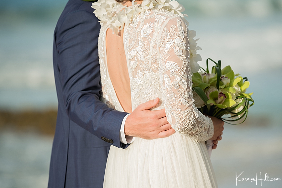 closeup of a groom holding his bride's waist during their wedding ceremony on the beach 