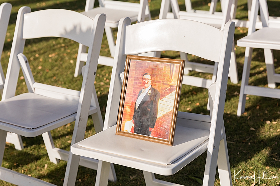 photo of a loved one who's passed is placed on a white chair at the front of the wedding ceremony 