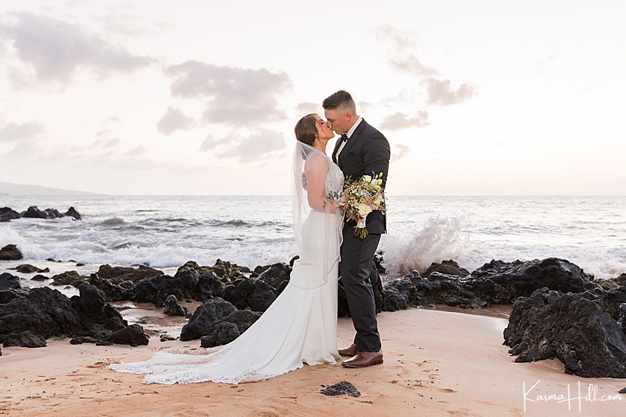 bride and groom kiss as the maui ocean splashes in the background 