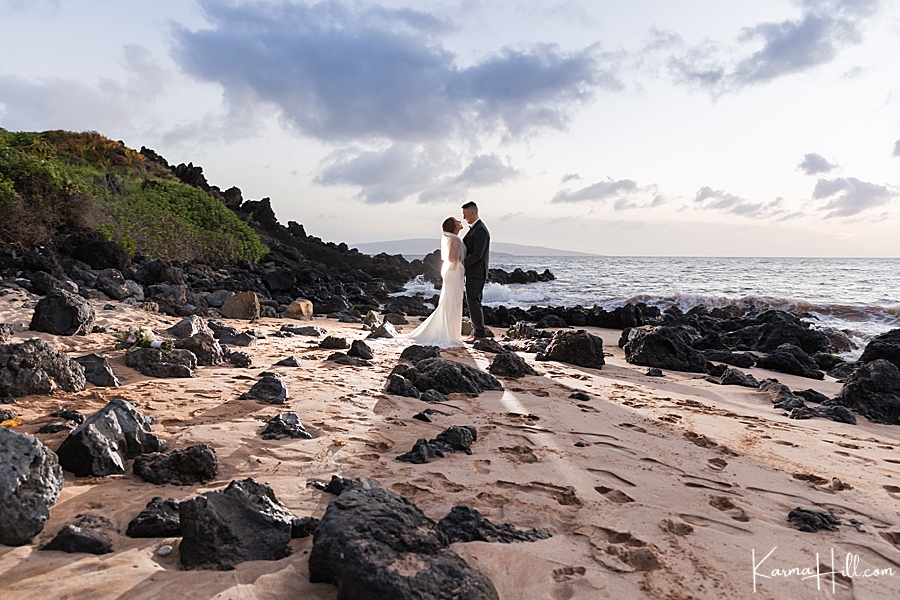 bride and groom pose on a rocky hawaiian beach with backlighting 