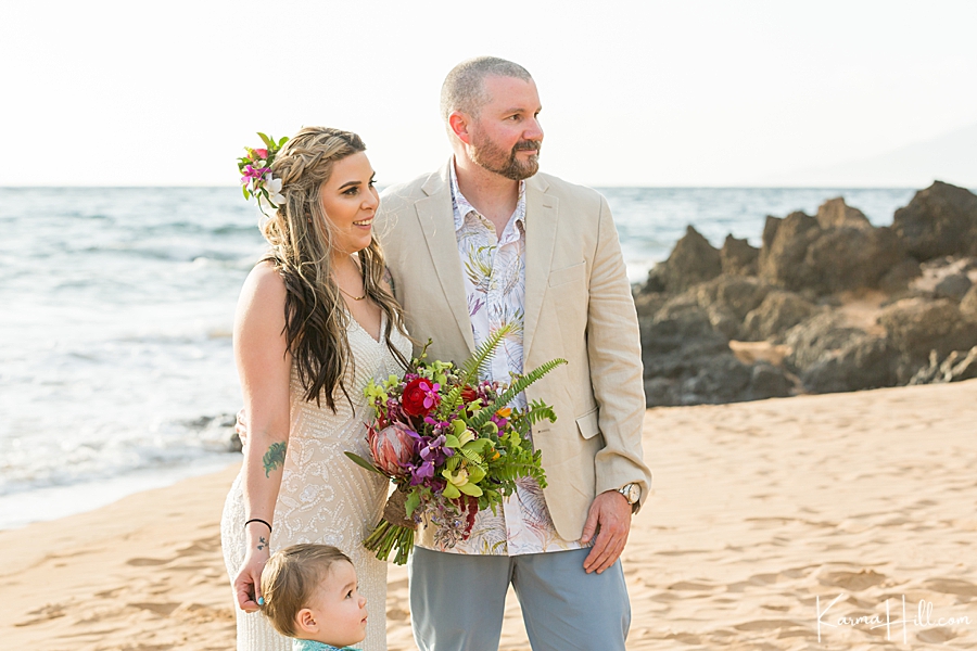 couple stand with their toddler during their maui beach wedding 