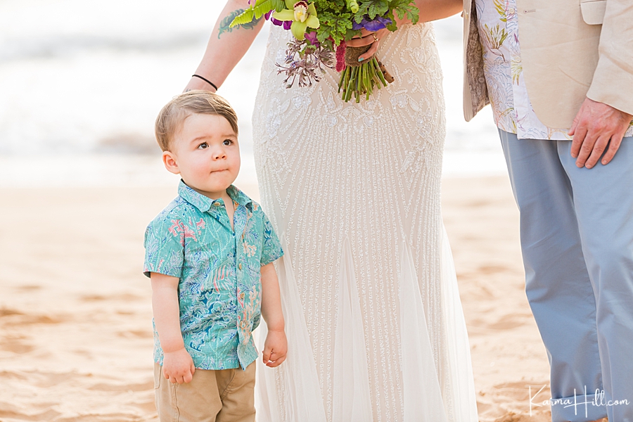 cute toddler wearing a blue aloha shirt watches as mom and dad get married on a beach in hawaii 