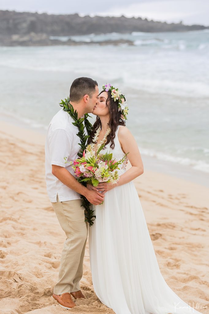 bride wearing a flower crown in hawaii on the beach with groom in maile lei 
