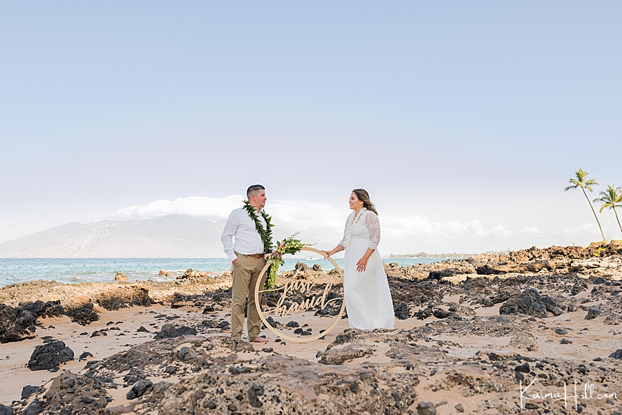 newlywed couple poses with a just mauid sign in front of the ocean 