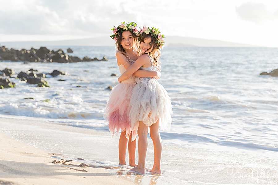 sisters hug on maui beach wearing fluffy dresses and flower crowns after parents' wedding 