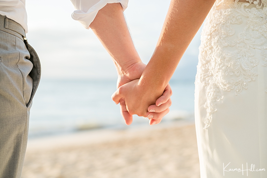 close up of bride and groom holding hands in front of a beach in hawaii 
