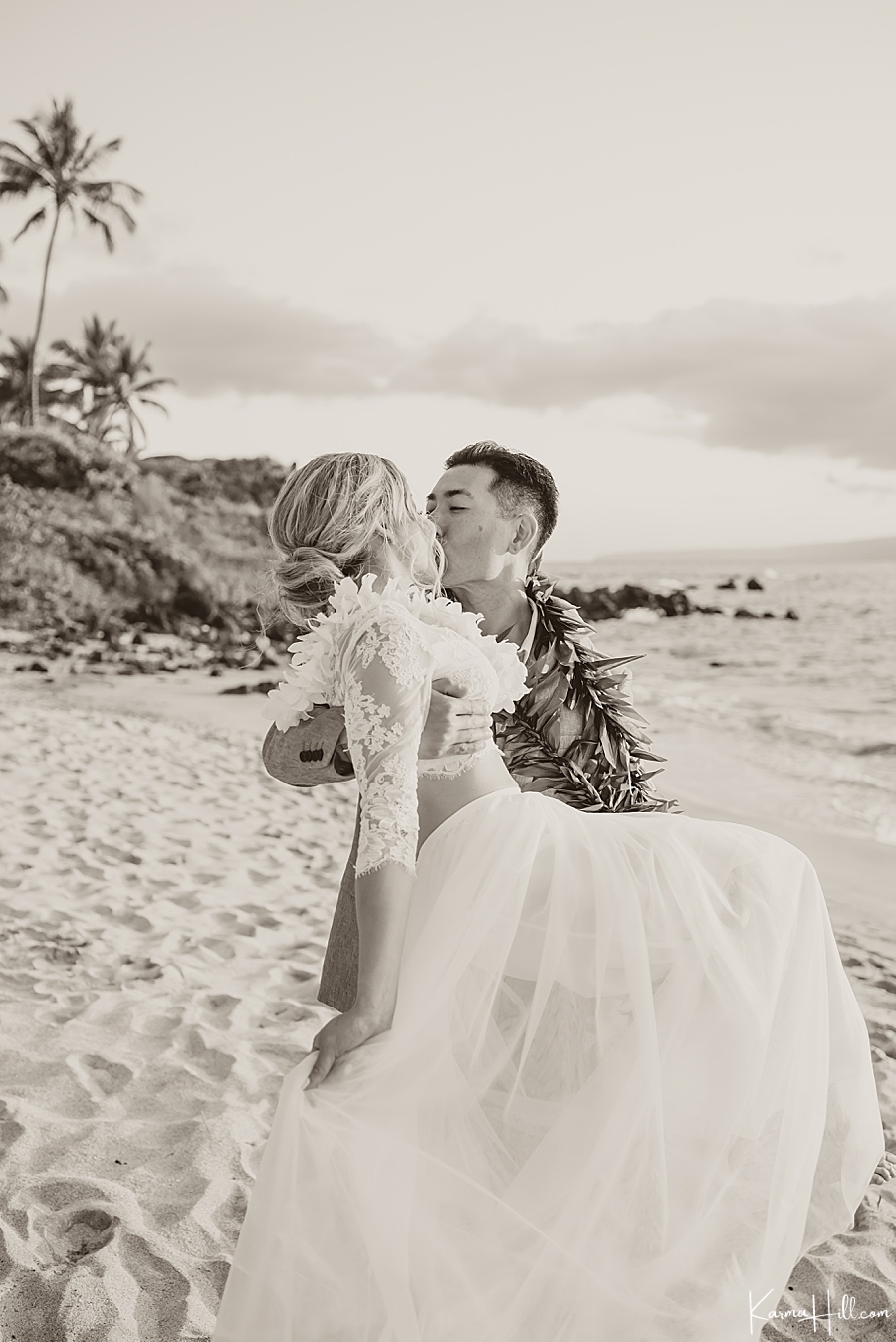 black and white image of a groom and bride with groom carrying the bride over the beach in hawaii 