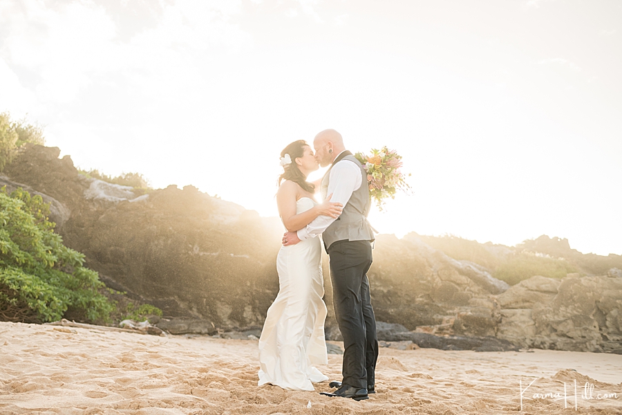 sun glowing behind bride and groom as they embrace on maui beach 