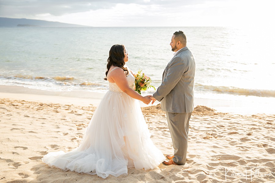 bride and groom stand while holding hands on hawaii beach 