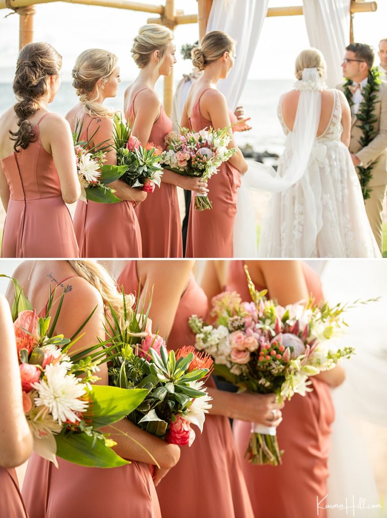 bridesmaids in coral line up in front of the ocean carrying hawaiian bouquets 