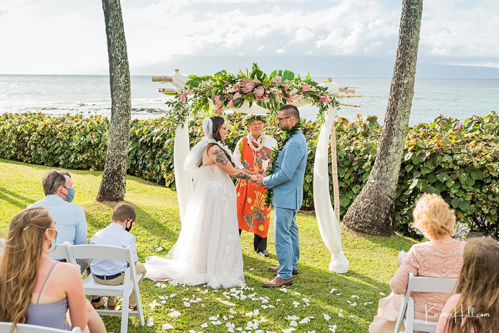 bride and groom stand with a hawaiian reverend in front of a wedding arch at merriman's in kapalua 