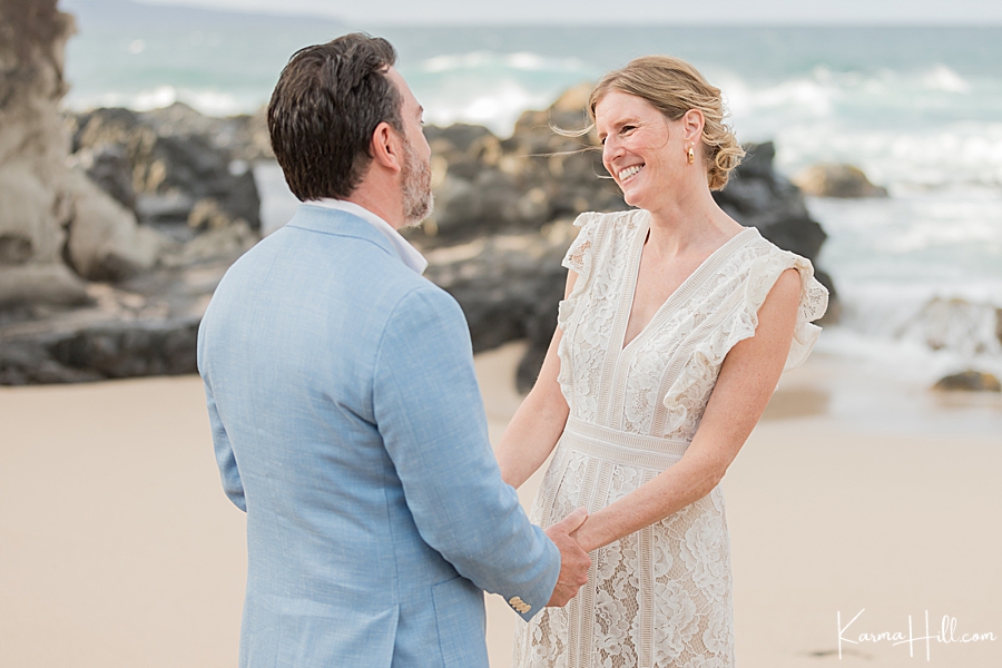 bride in bohemian dress and groom in french blue jacket hold hands during their beach wedding 