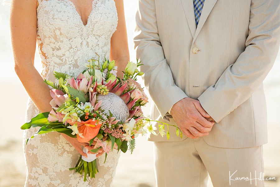 cropped image of a bride holding a tropical bouquet and a groom standing next to her in a beige suit