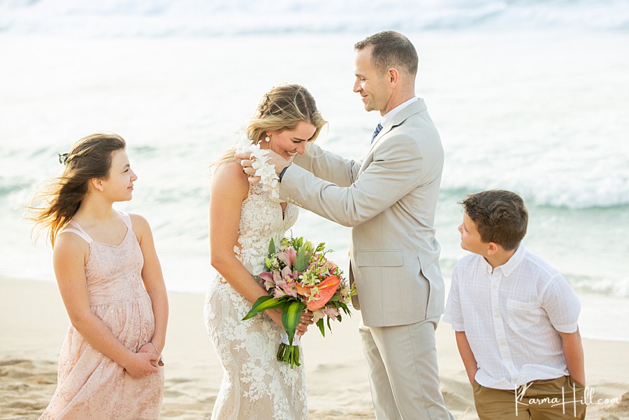 real moment when groom gives his bride a lei on the shore of a hawaiian beach 