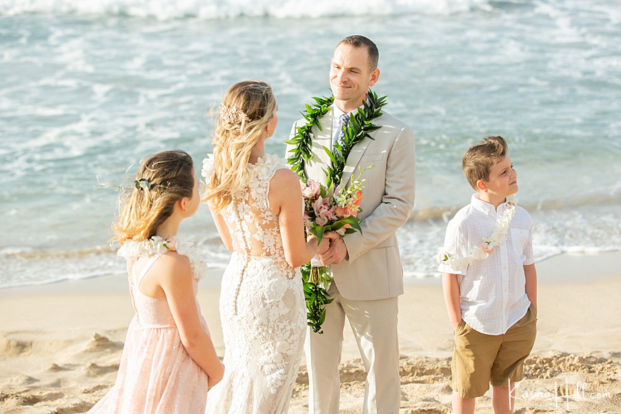 cute candid moment at a beach wedding in hawaii with the couple's children standing near 
