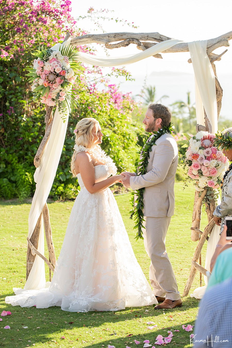 bride and groom stand in front of a driftwood arch with roses and exchange vows 