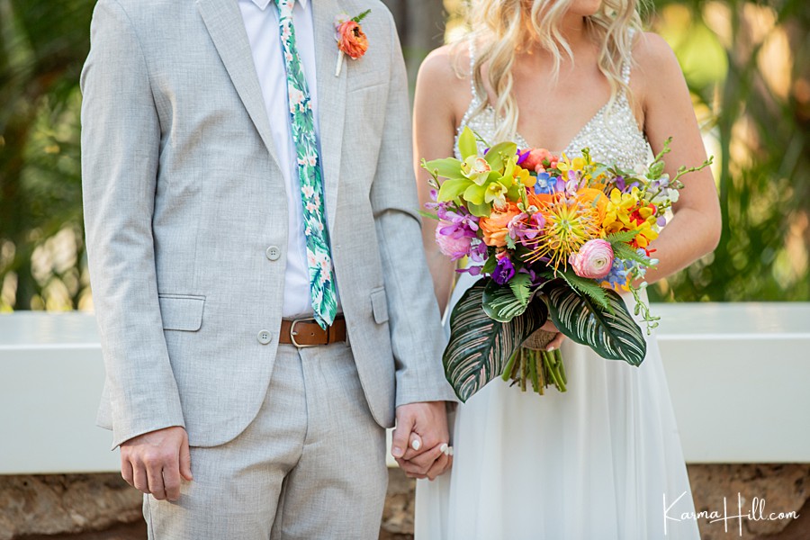 closeup of bride holding groom's hand and holding a tropical wedding bouquet 