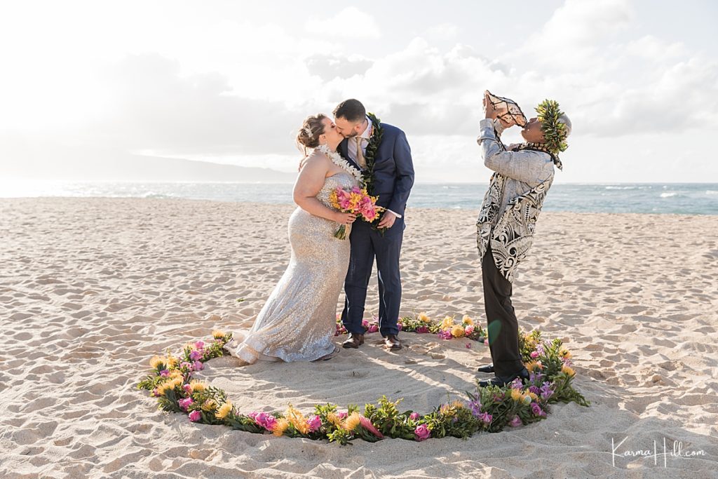 bride and groom kiss in a circle of flowers along the beach 
