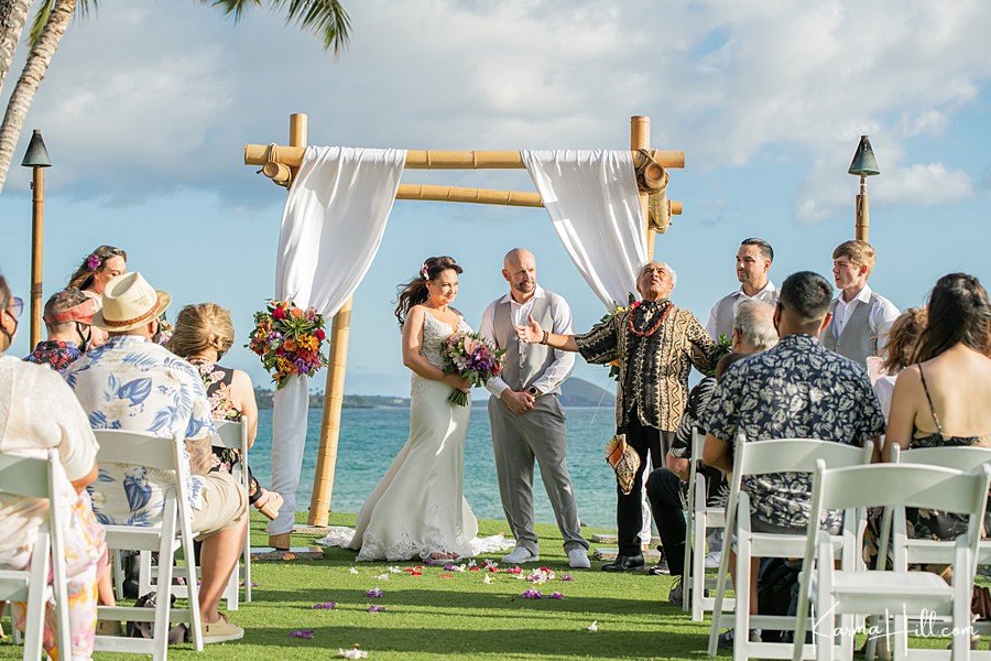 bride and groom stand beneath a bamboo arch as hawaiian minister opens the ceremony 