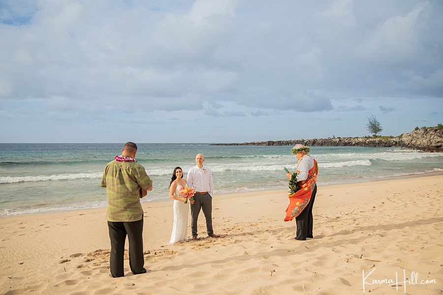 couple stand on a beach with a musician and hawaiian minister as they elope 