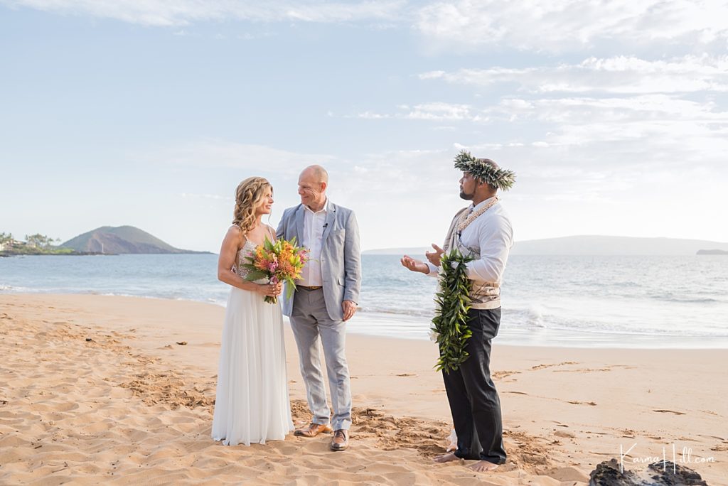 a couple stands on maui beach with a hawaiian minister for their elopement 