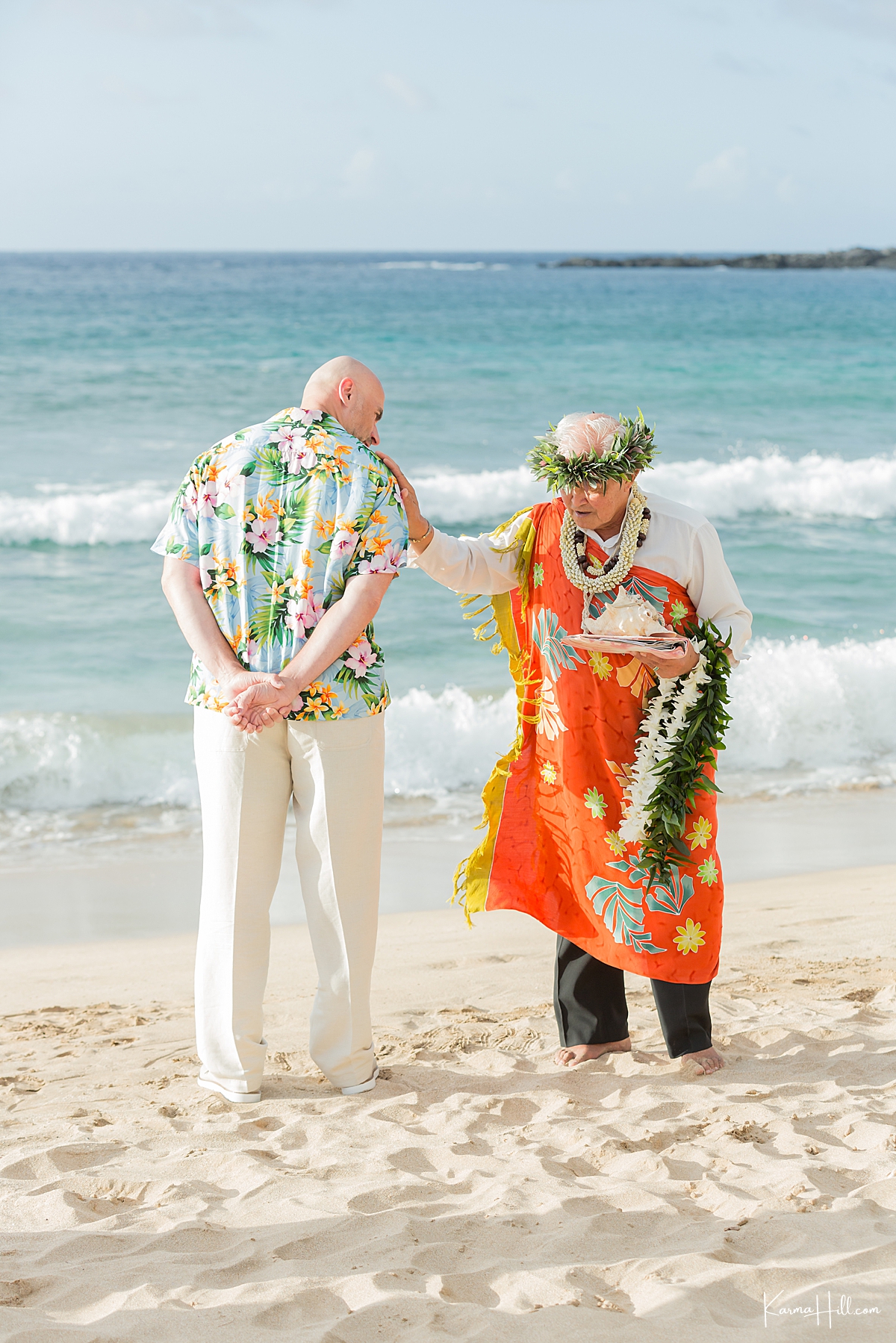 hawaiian minister puts his hand on grooms shoulder with the ocean in the background 