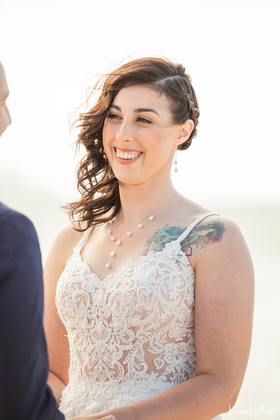bride with side part and braid with shoulder tattoo smiles at groom 