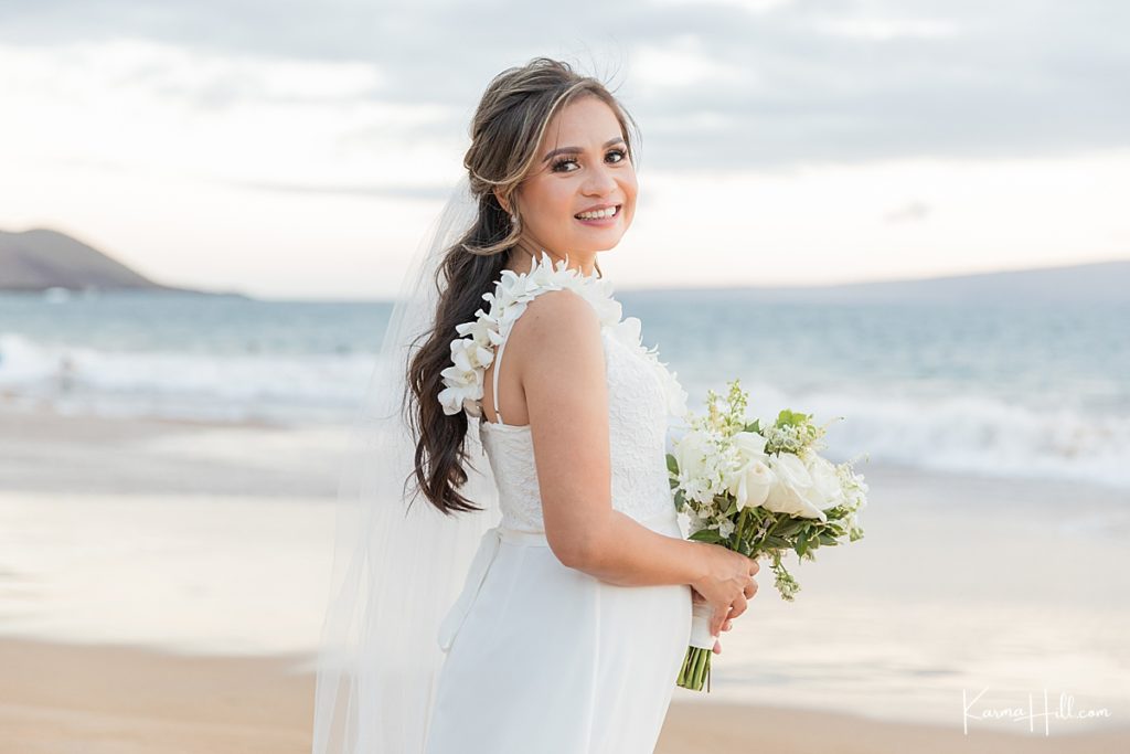 bride stands with white bouquet on maui beach 